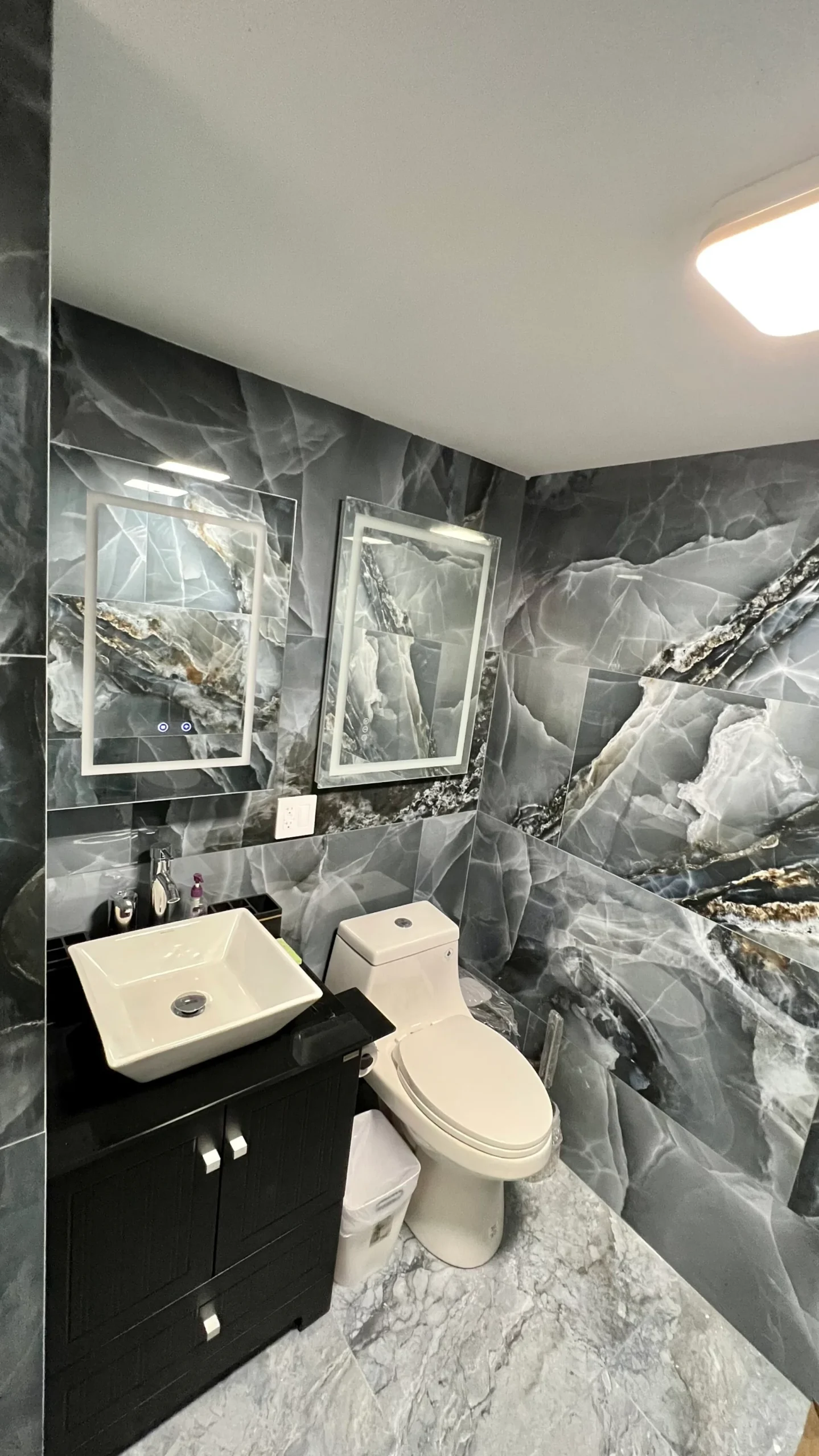 Completed bathroom with black vanity toilet mirror and dark marble-pattern tile in Salem Massachusetts