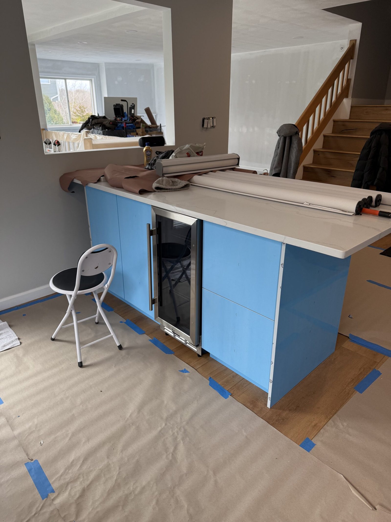 Glossy white kitchen island covered with blue protective film, white countertop, and appliance opening beside the stair in Salem Massachusetts