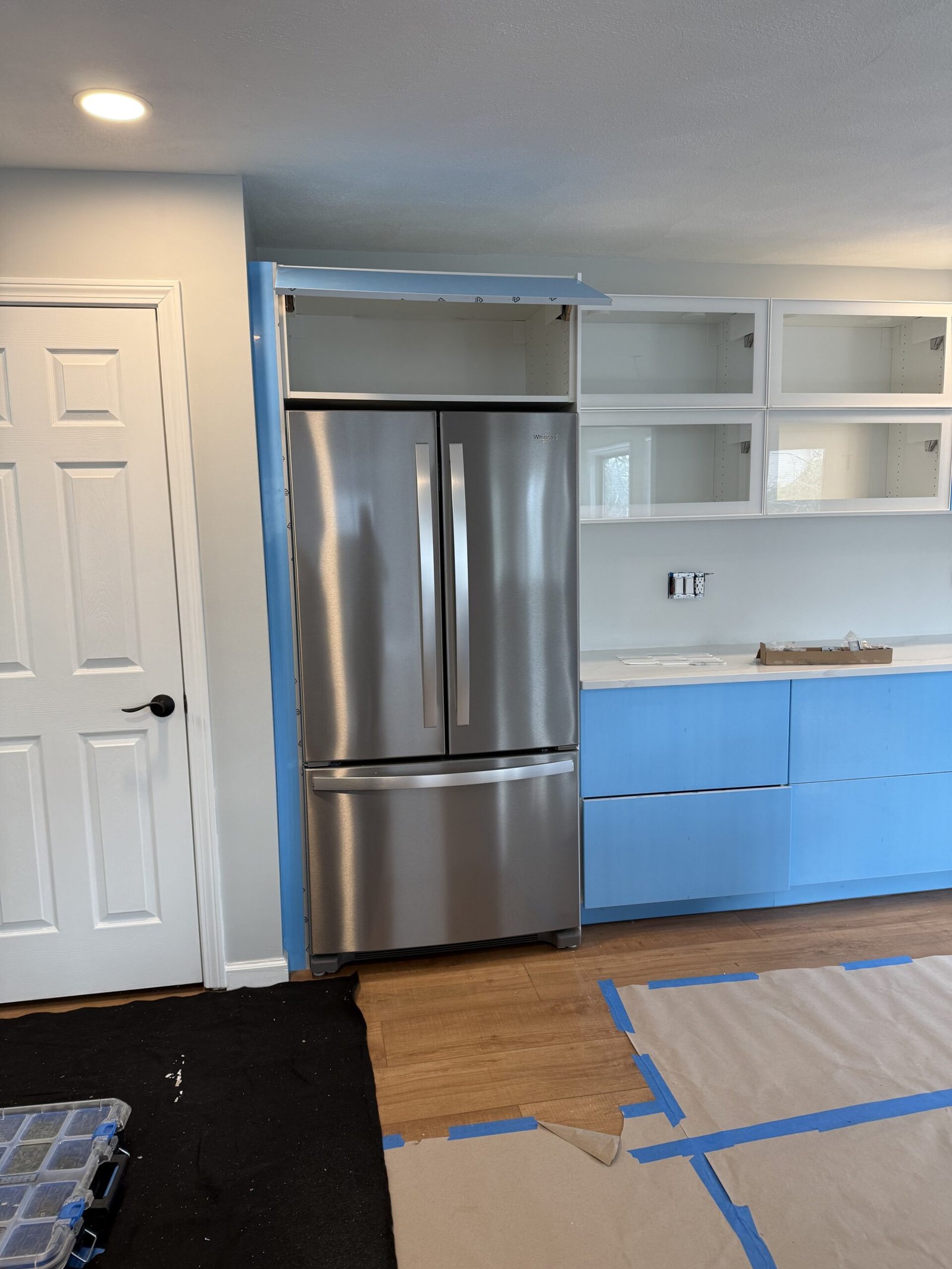 Stainless refrigerator glossy white cabinetry under blue protective film and doorway transition in a Salem kitchen remodel