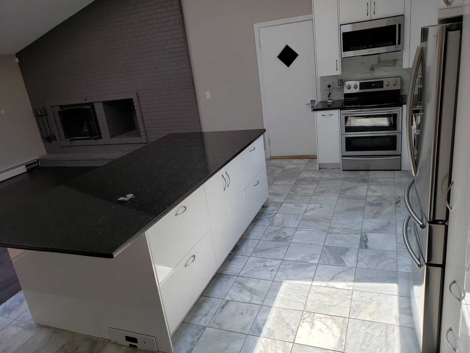 Completed white kitchen with dark countertops island stainless appliances and tile floor in Saugus Massachusetts