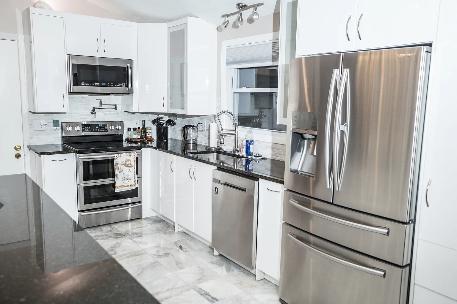 Finished Saugus kitchen with stainless appliances white cabinetry dark counters and tile floor