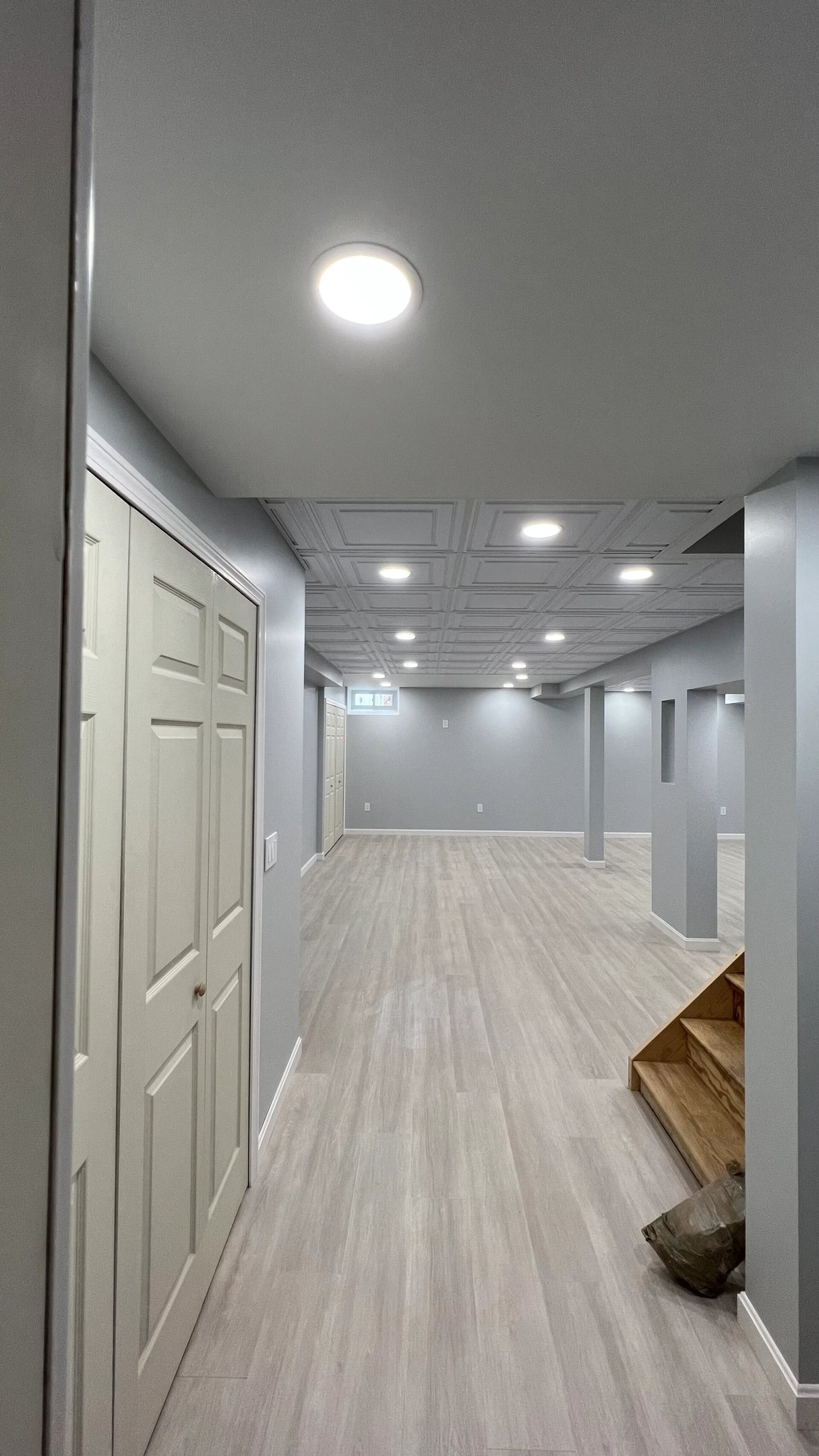 Completed Marblehead basement family room with light flooring, recessed lighting, decorative ceiling panels, closets, and finished columns
