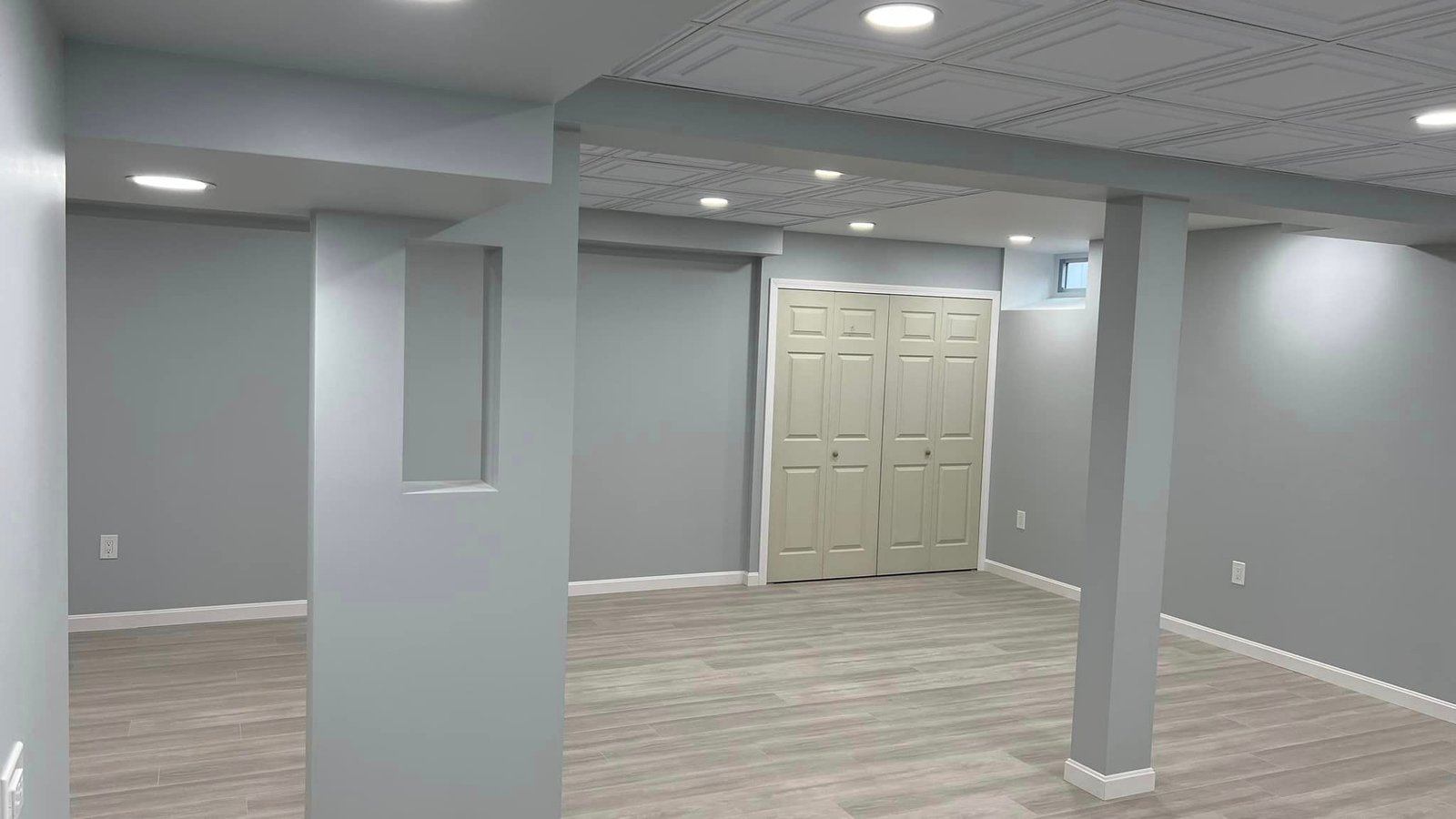 Wide completed view of the Marblehead basement with decorative ceiling panels, recessed lights, finished columns, doors, and flooring