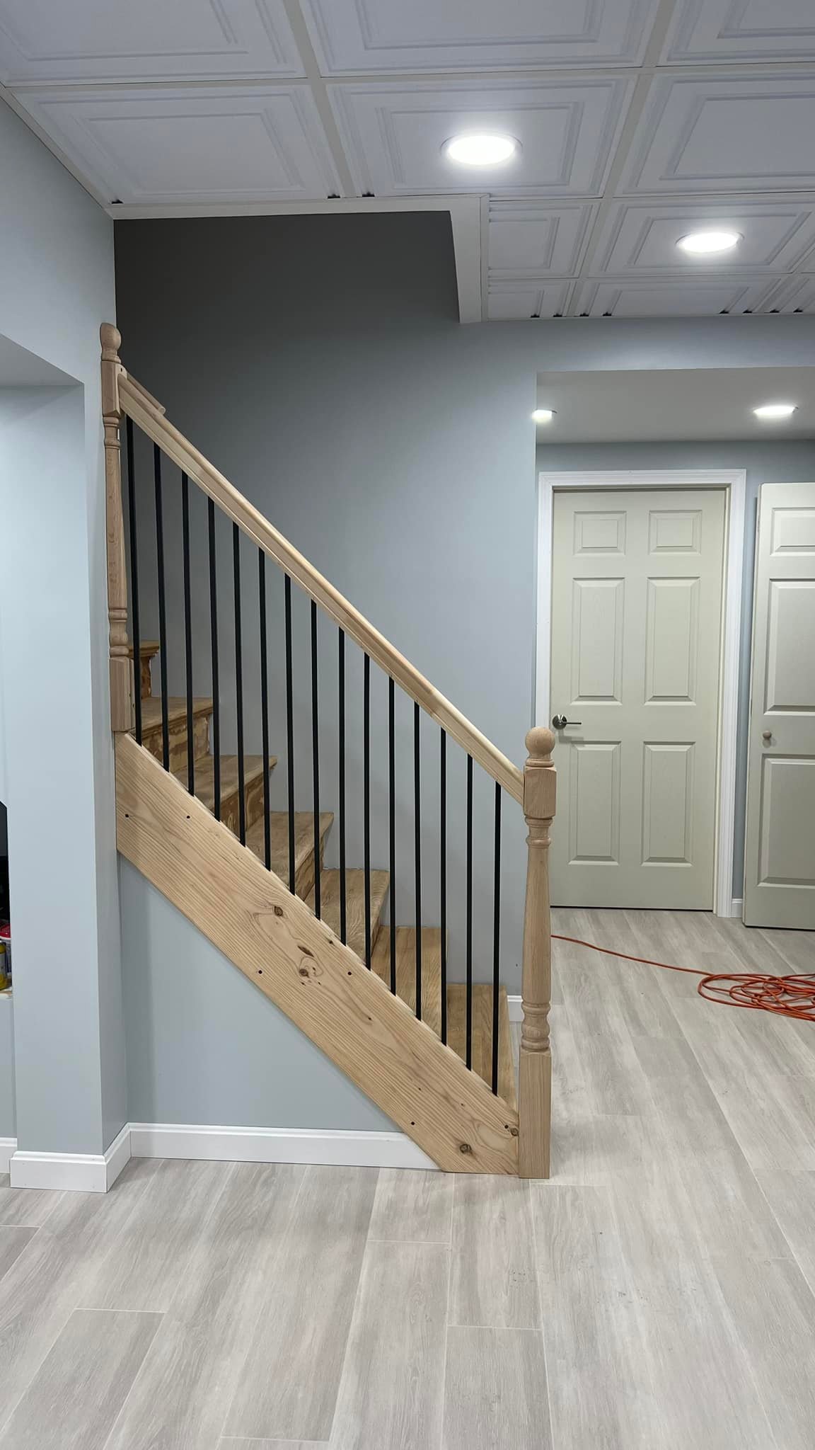 Completed basement staircase with wood handrail, black balusters, finished walls, trim, and nearby doors in Marblehead Massachusetts