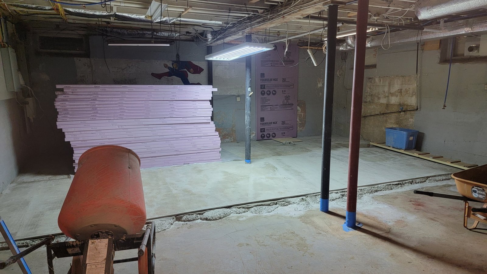 Open unfinished basement before the Marblehead renovation, with exposed ceiling, concrete floor, support posts, and insulation materials on site